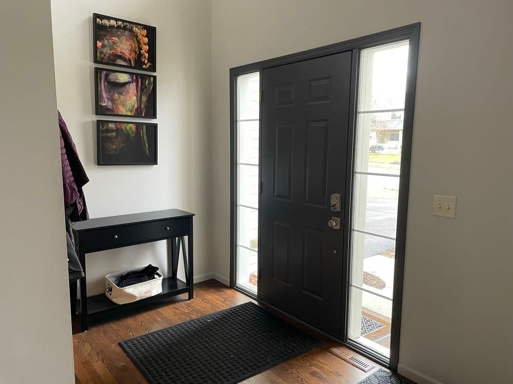 Modern entryway with black door, art, console table, and wooden flooring.