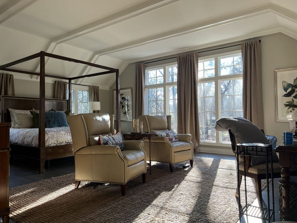 Cozy bedroom with four-poster bed, armchairs, large windows, and stylish decor.