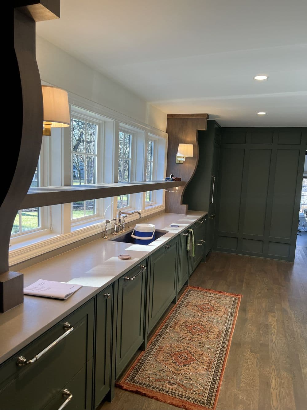 Modern kitchen featuring dark green cabinets, bright windows, and elegant design elements.