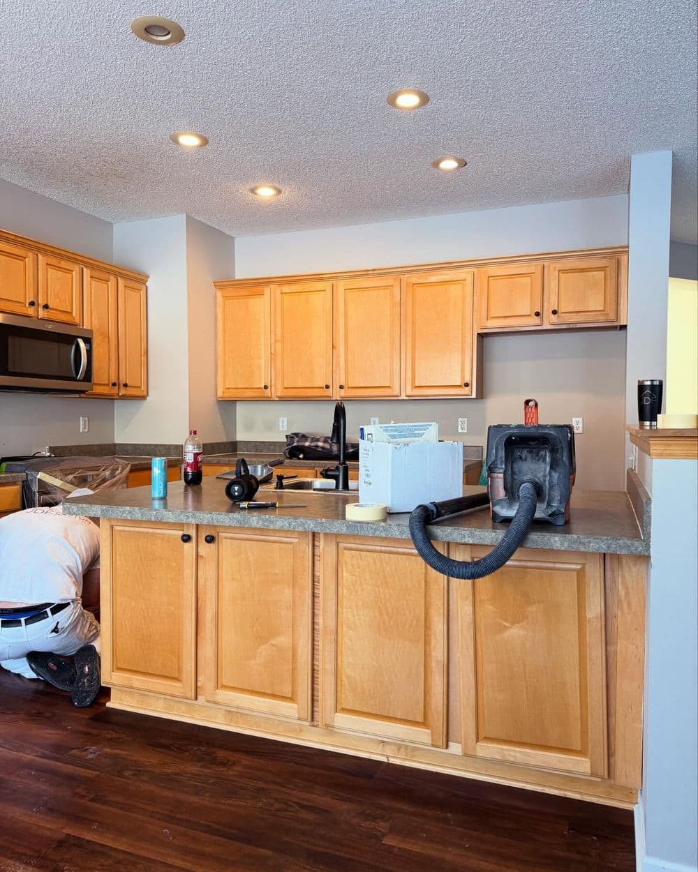 Renovated kitchen with wooden cabinets, countertop, and someone cleaning nearby.