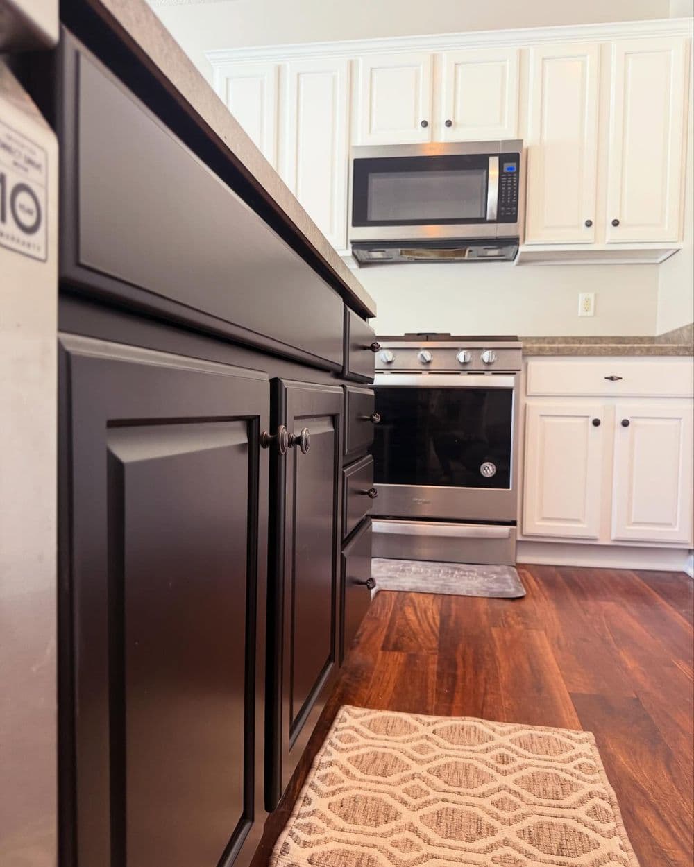 Modern kitchen with black cabinets, stainless steel oven, and wood flooring. Cozy area rug visible.