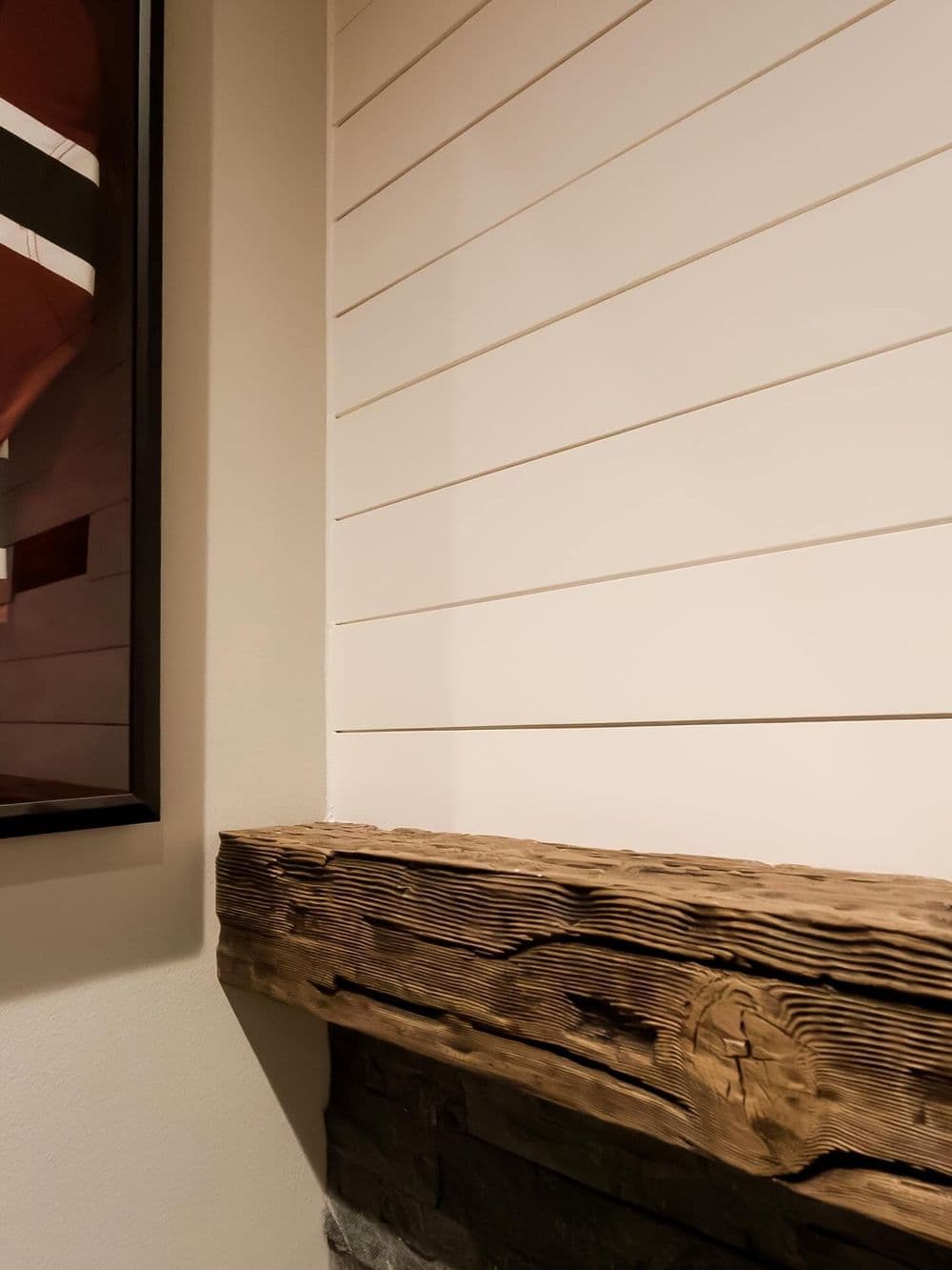 Rustic wooden mantel above stone fireplace with white shiplap wall background.