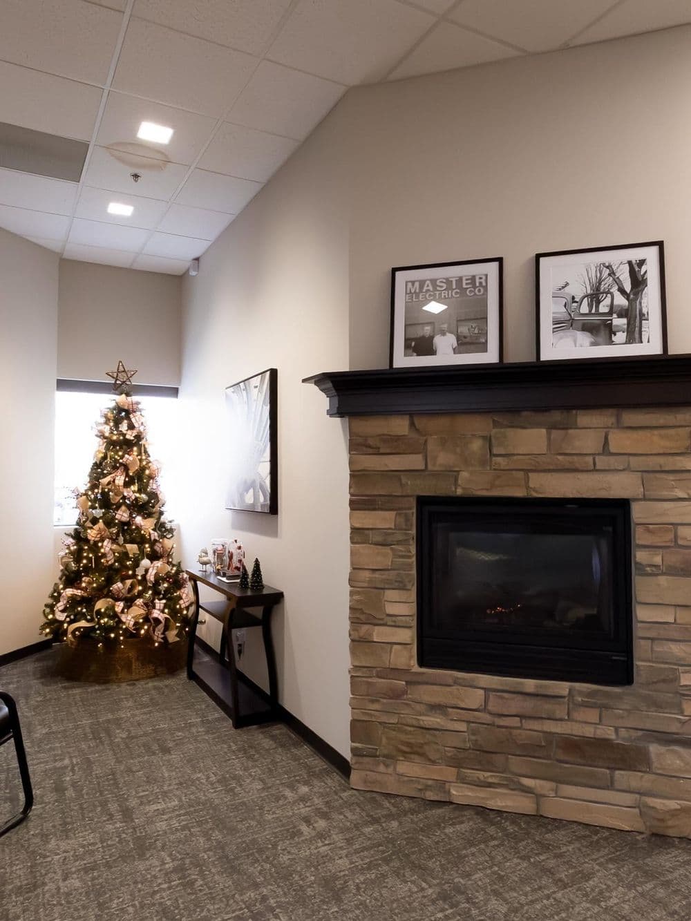 Christmas tree decorated with lights and ornaments next to a cozy stone fireplace in an office.