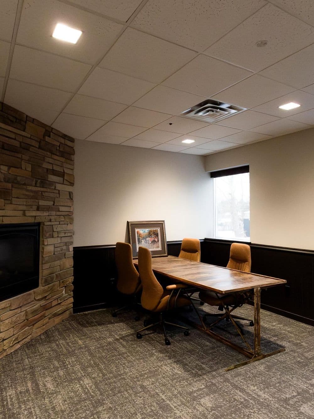 Modern conference room with wooden table, upholstered chairs, and stone accent wall.