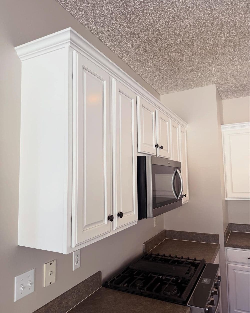 Modern kitchen cabinetry with white finish, stainless steel microwave, and dark knobs.