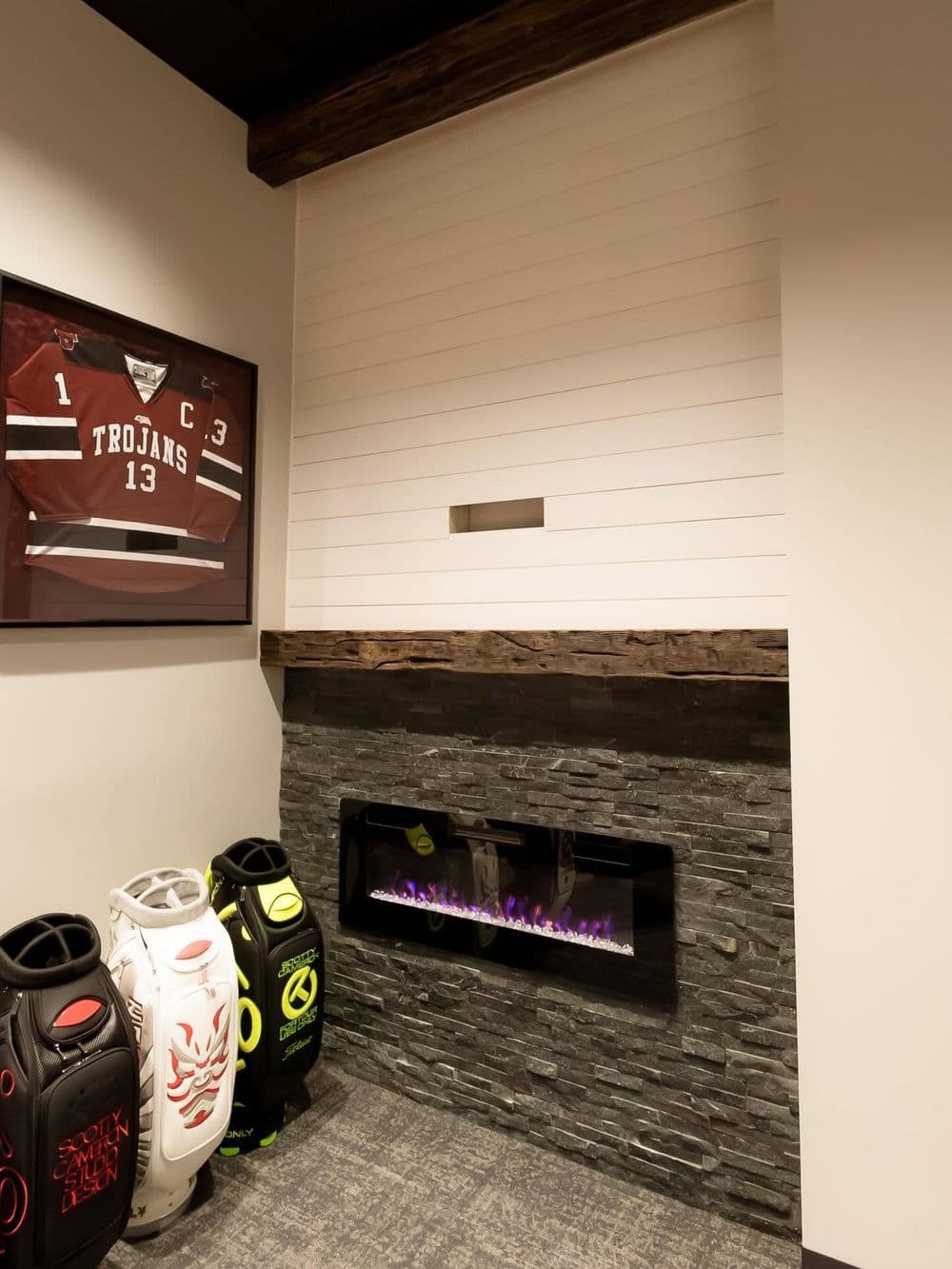 Trojans jersey displayed above modern stone fireplace with colorful golf bags nearby.