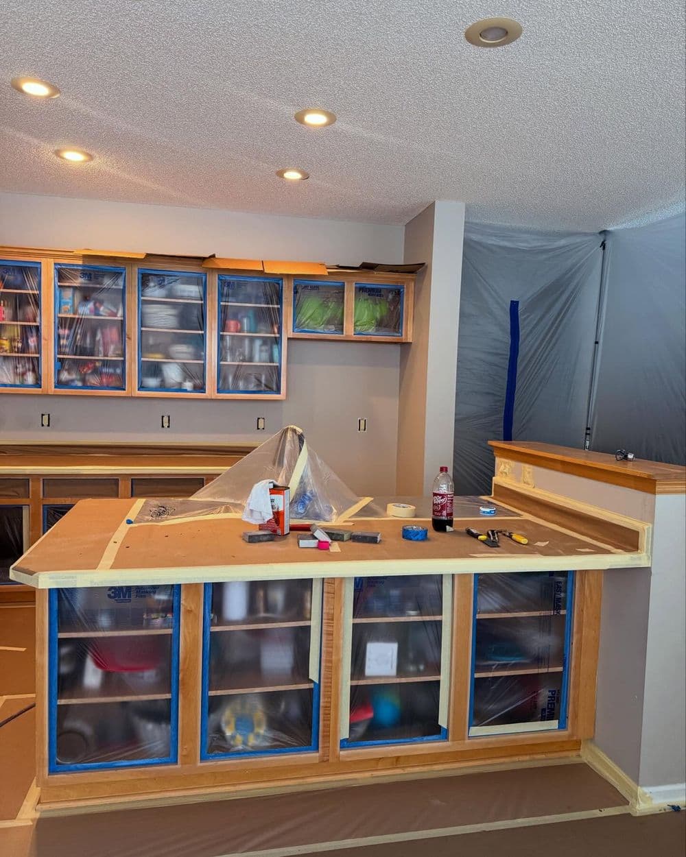 Kitchen renovation in progress with cabinets covered and construction materials visible.