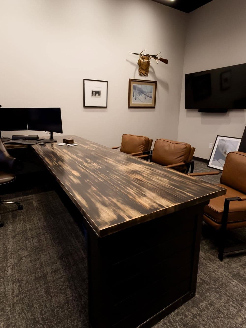 Modern office setting with a rustic wooden table, leather chairs, and digital screens.