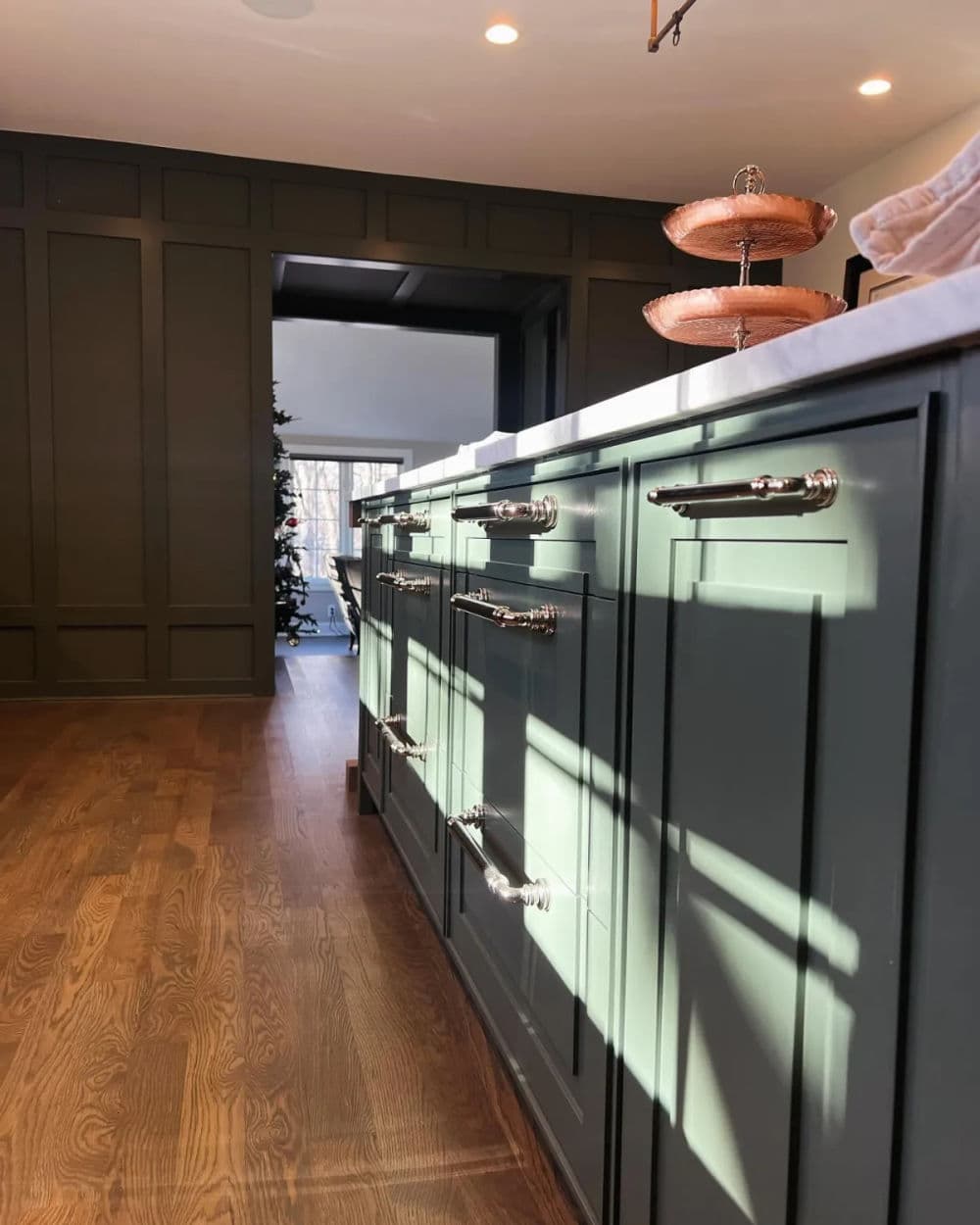 Modern kitchen with green cabinets, silver handles, and warm wood flooring, bathed in natural light.